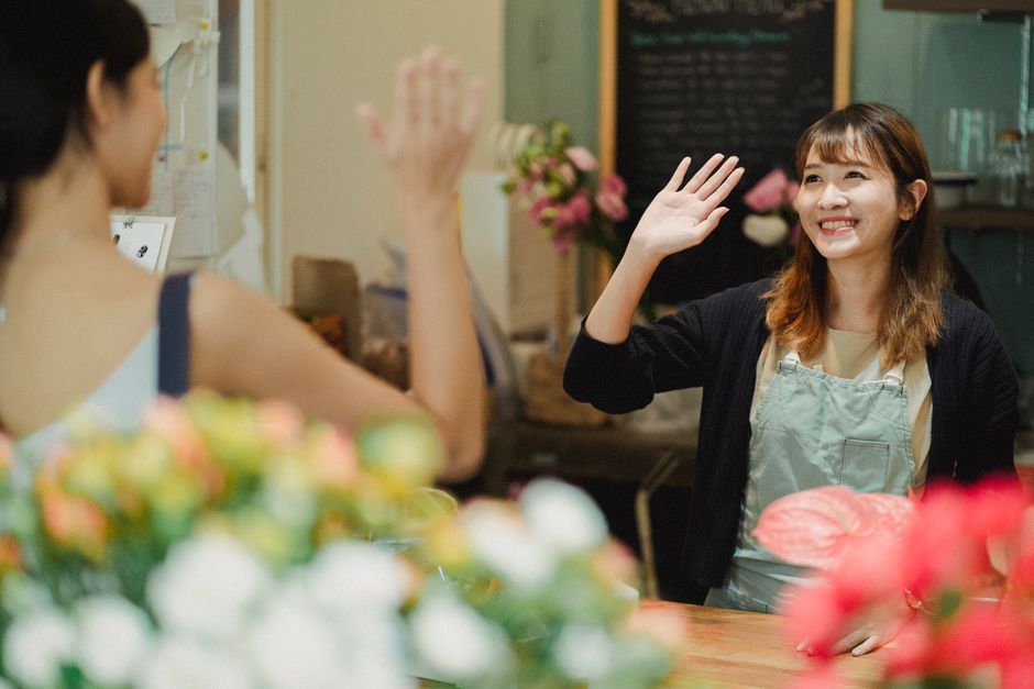 A florist at floristarchway.co.uk shares a friendly moment with a customer at the floral shop near Whittington Hospital Archway. The florist, a young woman with shoulder-length brown hair, is smiling 