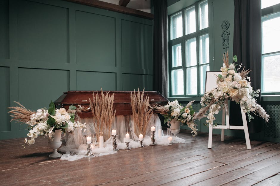A floral arrangement featuring predominantly white flowers, including roses and orchids, complemented by soft beige pampas grass. The flowers are arranged in white vases and placed on the floor alongs